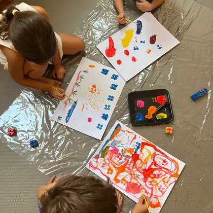 Crianças pintando com as mãos sobre papéis no chão, na aula de Artes e Movimento
