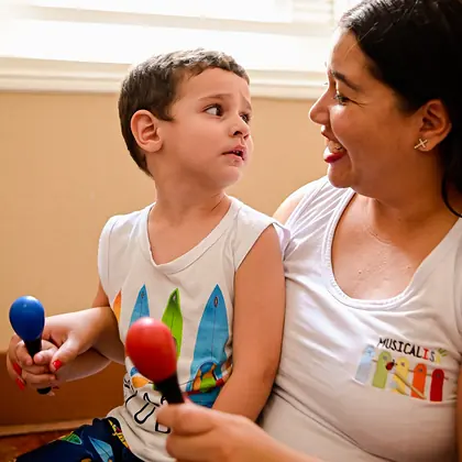 Menino segurando maracas ao lado da musicoterapeuta
