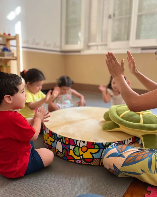 Crianças batem palmas em volta de um tambor na aula de musicalização infantil do Musicalisa, em Mococa