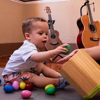 Menino pequeno brinca com ovinhos musicais ao lado de violões