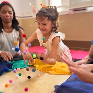 Menina ri brincando com pompons coloridos sobre o tambor